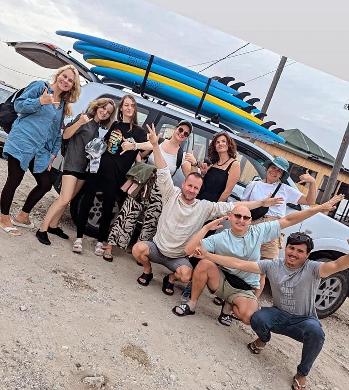 Grupo de surfistas y monitores junto a un SUV con tablas soft-top en el techo — escuela de surf en Essaouira, Marruecos