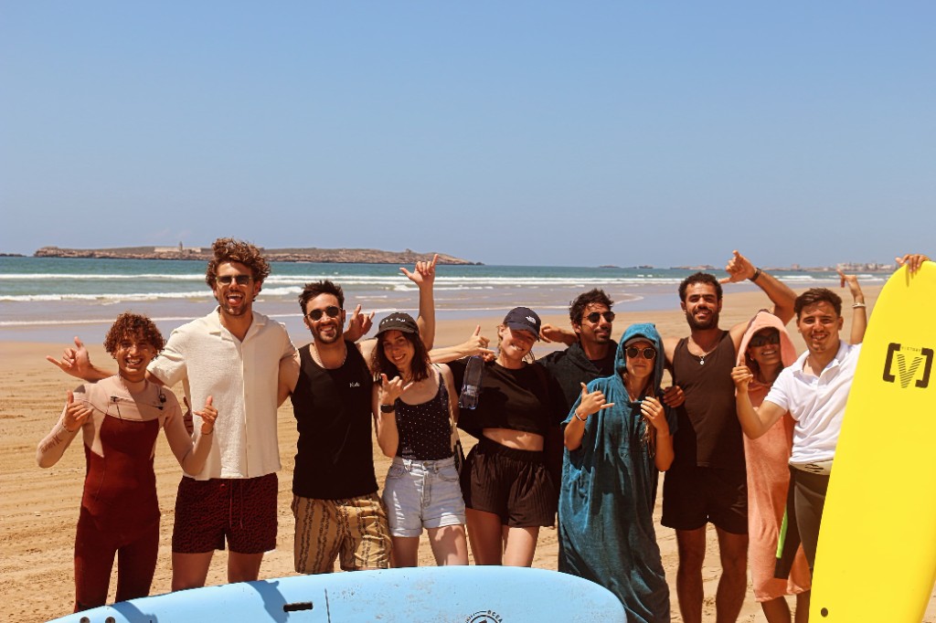 Participantes llevando tablas azules en la playa antes de una clase de surf en Essaouira.