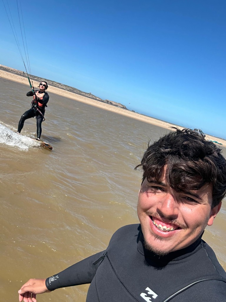 Monitor en selfie durante sesion de kitesurf con alumna al fondo en Essaouira.