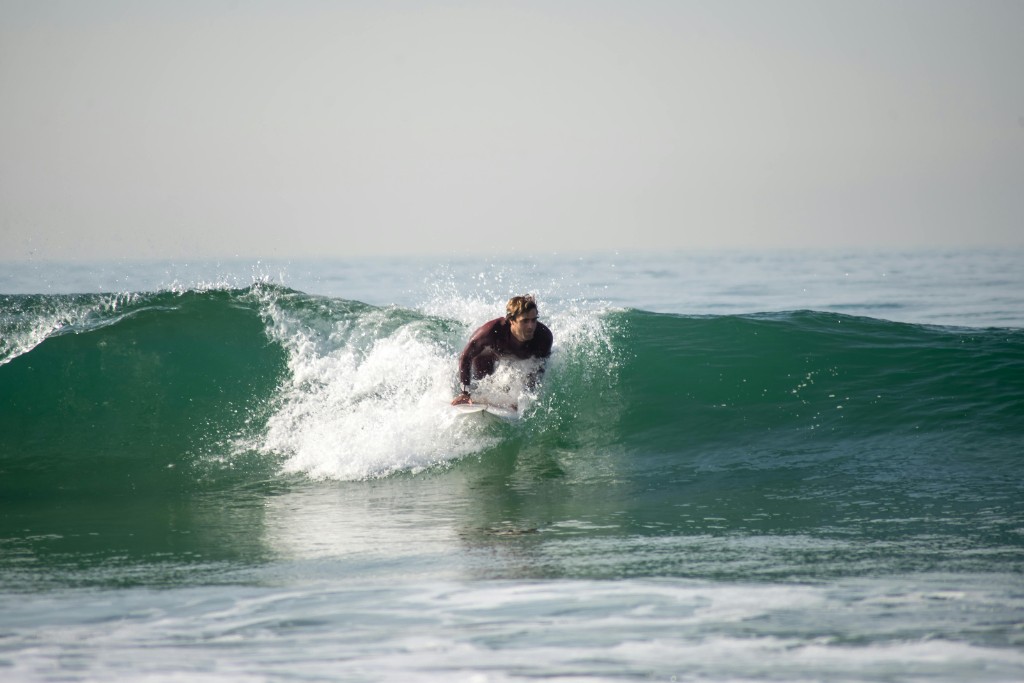 Alumna en equilibrio sobre una ola pequeña cerca de la orilla durante clase de surf en Essaouira.