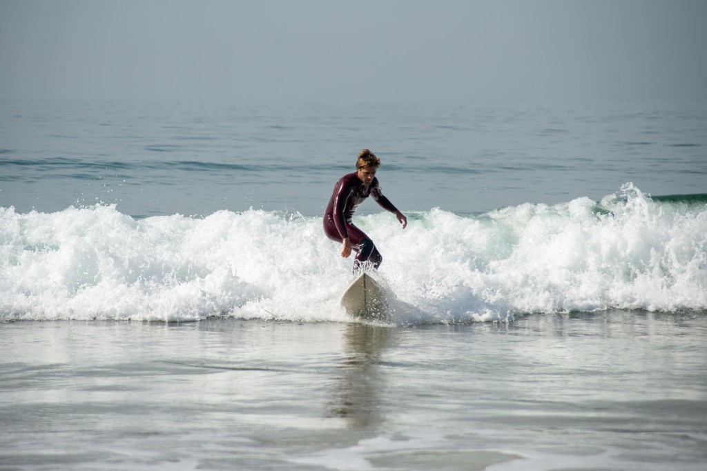 Surfista en neopreno en ola pequeña, postura baja — sesión surf bahía Essaouira.
