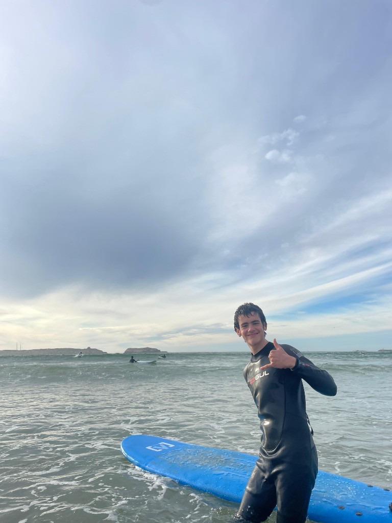 Surfista en el mar hasta la cintura, shaka y tabla soft azul — sesión surf Essaouira.