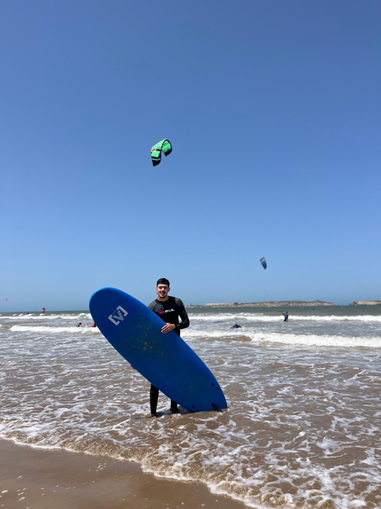 Surfista en la playa con cielo azul y bahía de Essaouira.