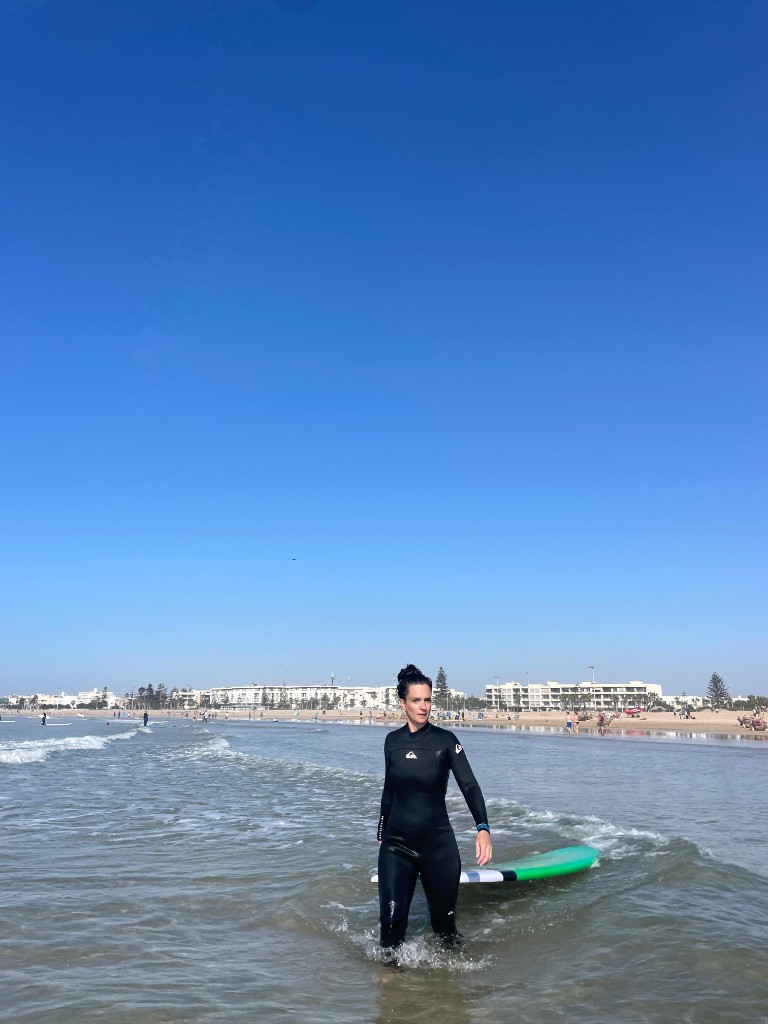 Surfista en neopreno en agua poco profunda con tabla verde — clase surf bahía Essaouira.